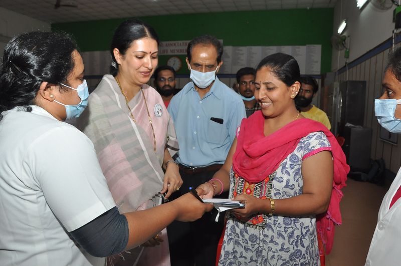A nurse hands a booklet to a woman at a hospital counter as trust representatives look on.