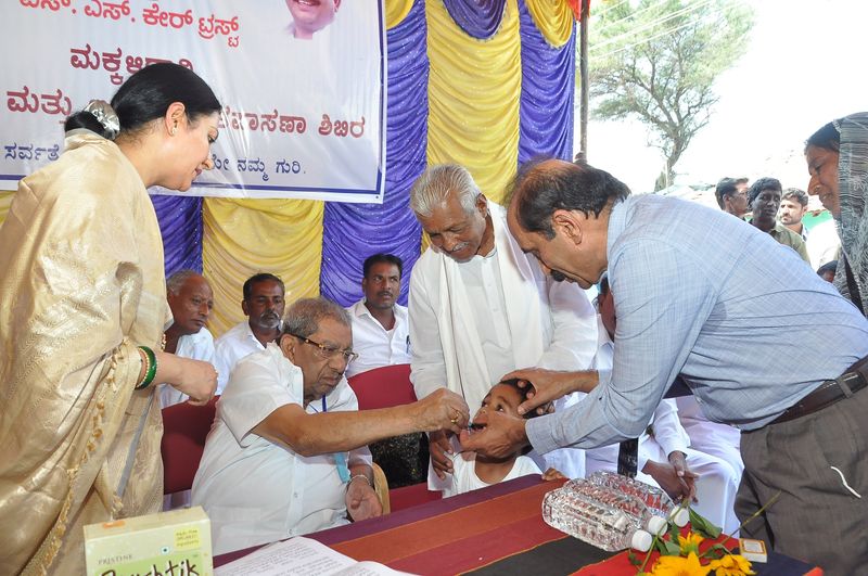 Doctors give drops to a young child at a health camp as elders look on.