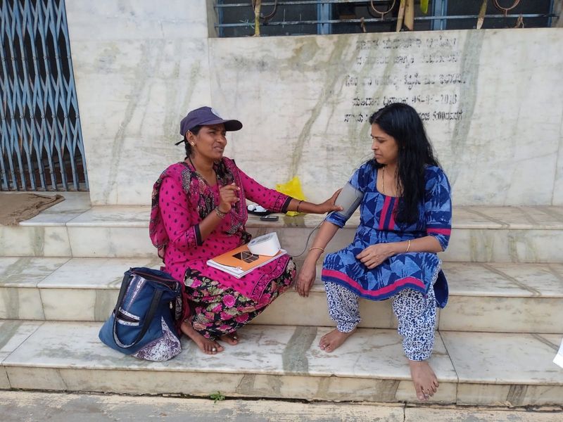 A health worker measures a woman's blood pressure on the steps of a village building.