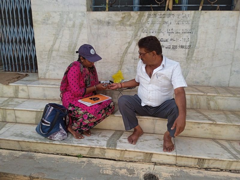 A health worker checks a man's blood sugar on the steps of a village building.