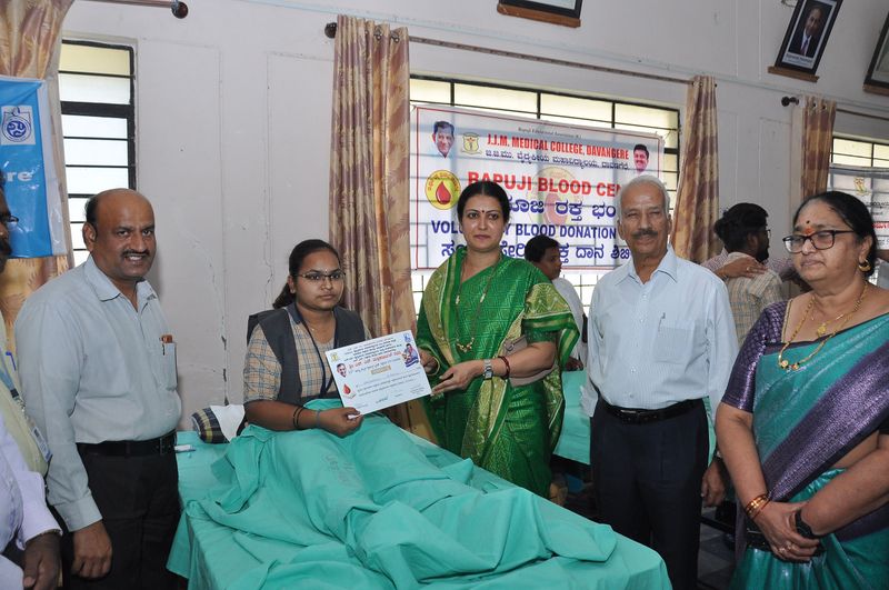 A blood donor holds up her certificate beside trust representatives at Bapuji Blood Centre.