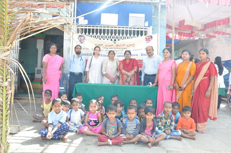 Health workers and anganwadi staff stand behind a group of young children at an anganwadi centre.