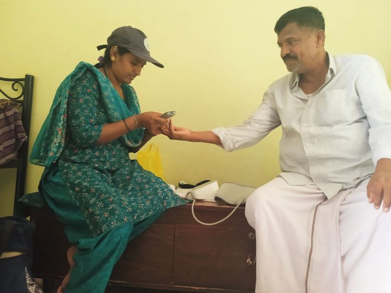 A community health volunteer checks a man's blood pressure during a home visit.