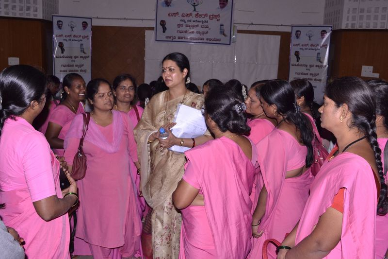 A trust representative speaks with health workers in pink uniforms at the cancer awareness campaign.