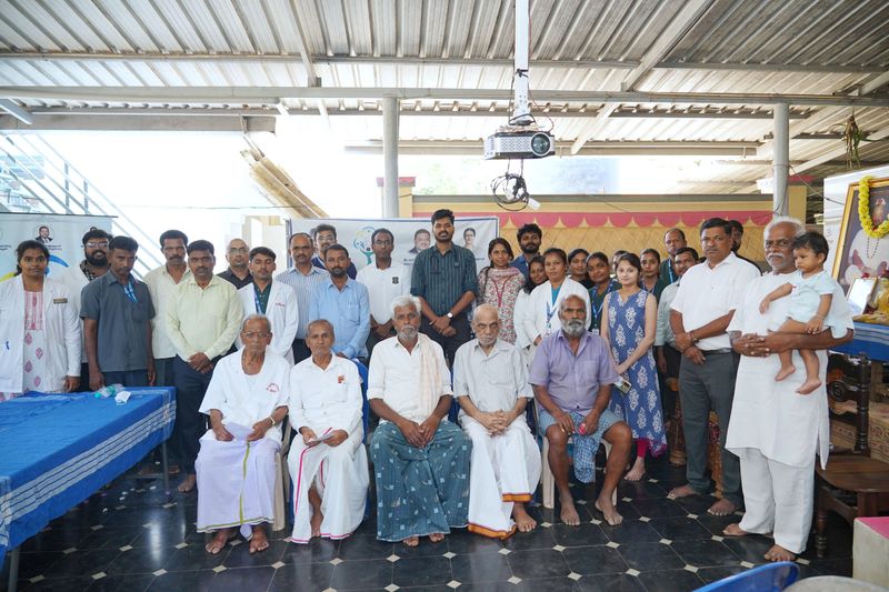 Elderly men sit in front of doctors and volunteers for a group photo at a Sanjeevini camp.