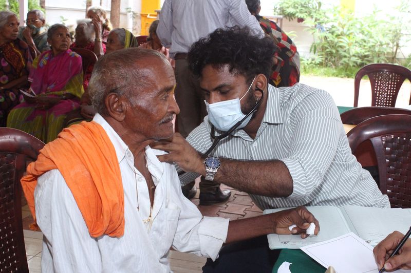 A doctor listens to an elderly man's chest with a stethoscope at a senior citizens' camp.