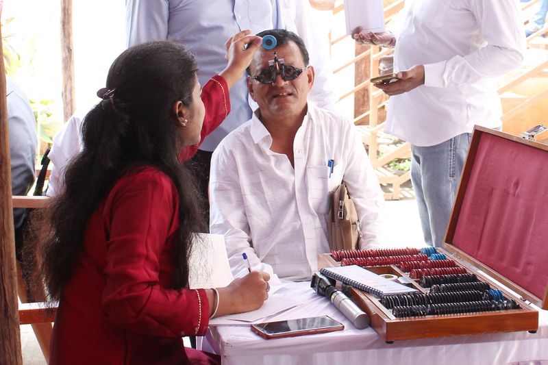 An optometrist tests a man's eyesight with a trial frame and lens set at a Health-on-Wheels camp.