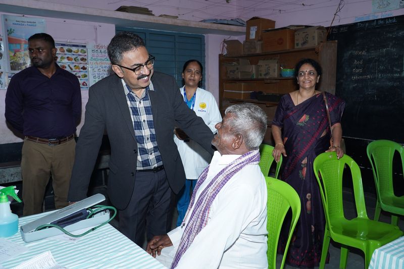 A doctor greets an elderly man waiting for his check-up at a Health-on-Wheels camp held in a village school classroom.