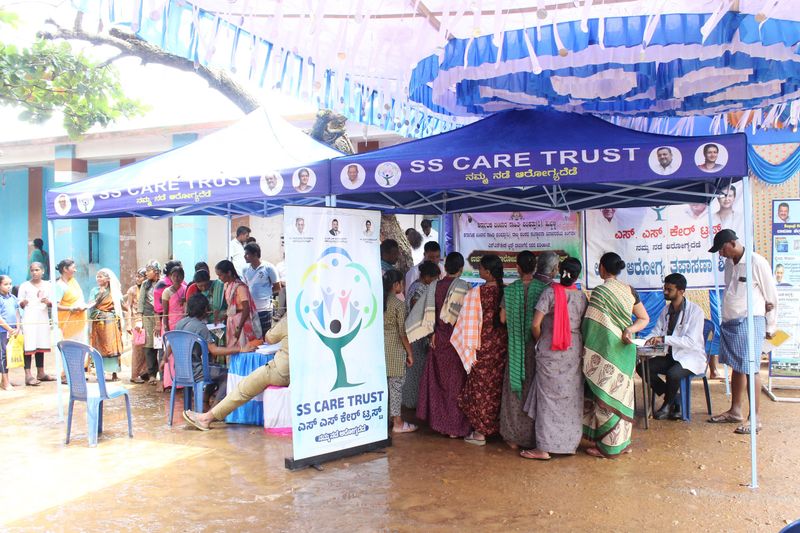Villagers line up under SS Care Trust canopies for registration and check-ups at a Health-on-Wheels camp.