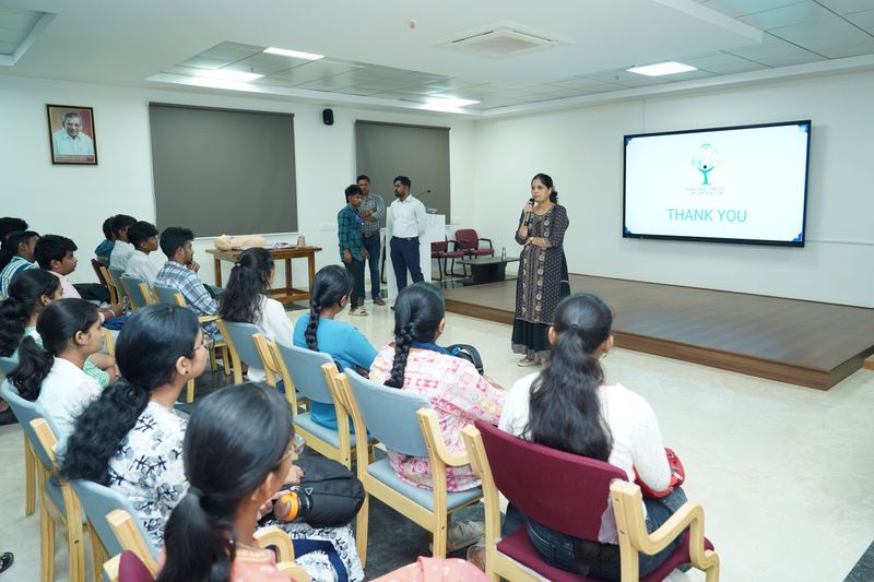 A speaker addresses a seated audience of young women at the close of a first aid training session.
