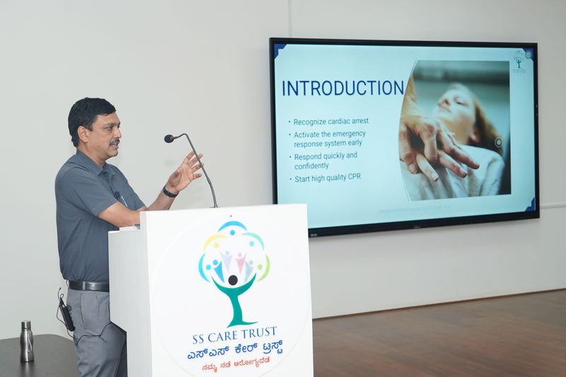 A facilitator stands at a podium beside a screen titled Introduction, explaining cardiac arrest response steps.
