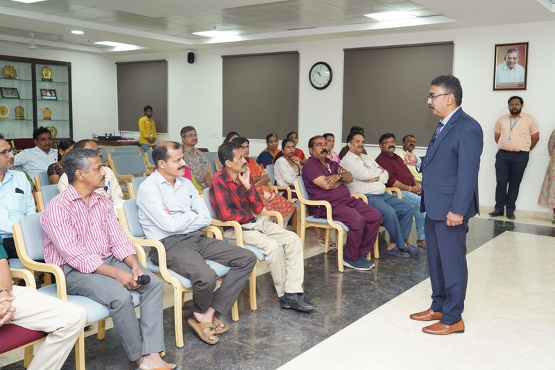 A speaker in a suit addresses a seated group of adults in a conference room during a community health training session.