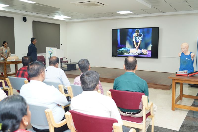 Seated participants watch a video demonstration of CPR technique on a large screen during a life-support training session.