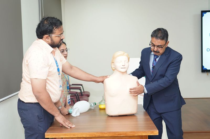 Two trainers and a participant examine a training mannequin and resuscitation bag used for airway management practice.