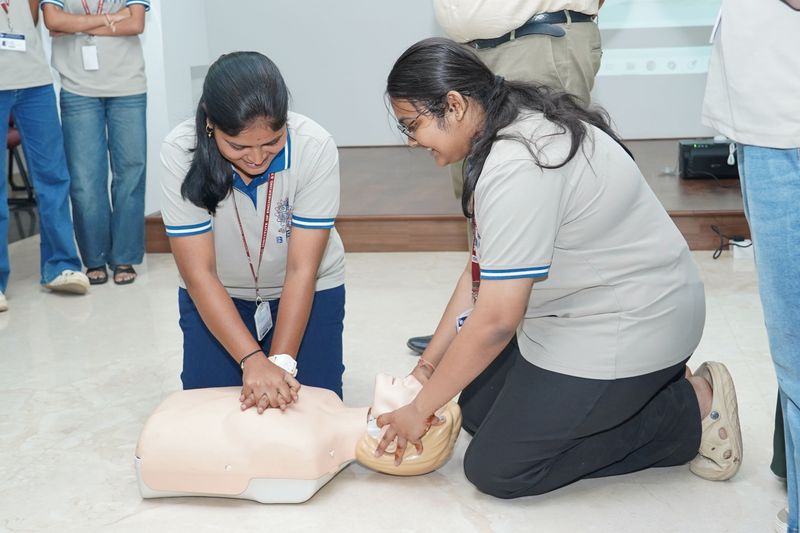 A trainer holds up a child-sized resuscitation mannequin while explaining its use to a group of students and staff.