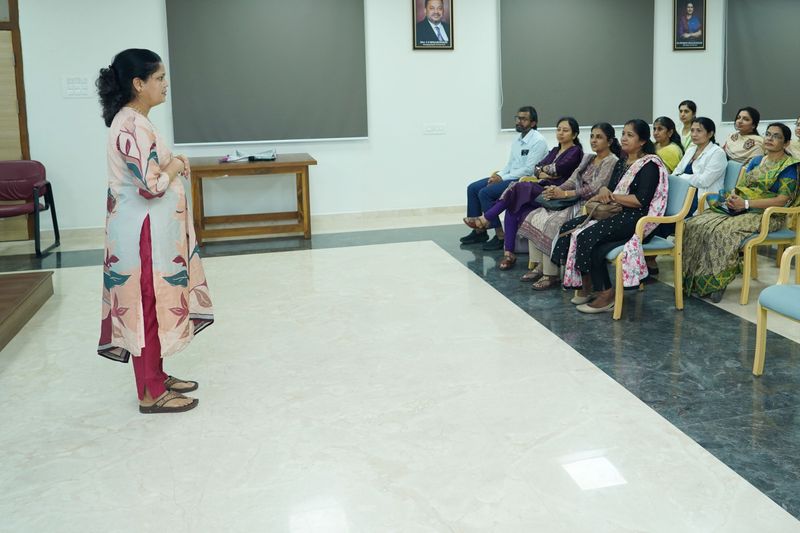 Woman trainer speaking to a seated group of women during a first aid awareness session in a small hall.