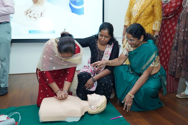 Three women in traditional sarees practising hands-on CPR technique on a training manikin.