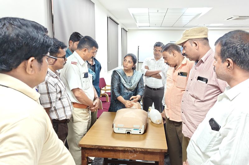 Group of participants gathered around a table examining a first aid training device during a workshop.