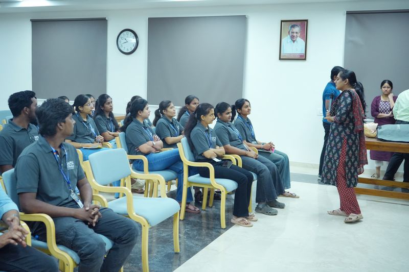 A group of young women in uniform sit and listen as a facilitator addresses them during a health training session.