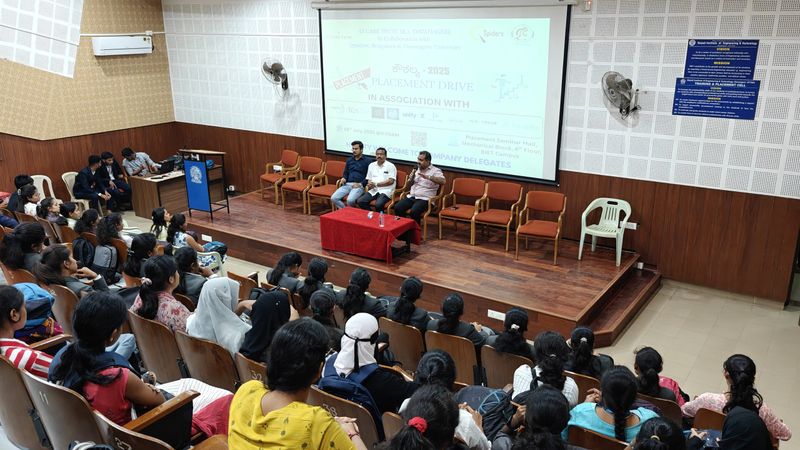 College students in a seminar hall face a stage where three speakers sit below the projected Kaushalya 2025 Placement Drive slide.