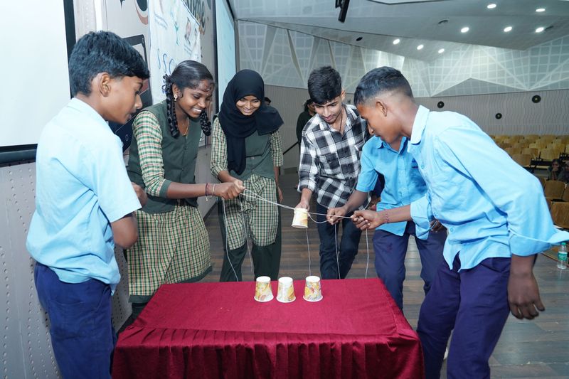 Students and young facilitators work together on a string-and-cup teamwork challenge during a Kaushalya skills session.