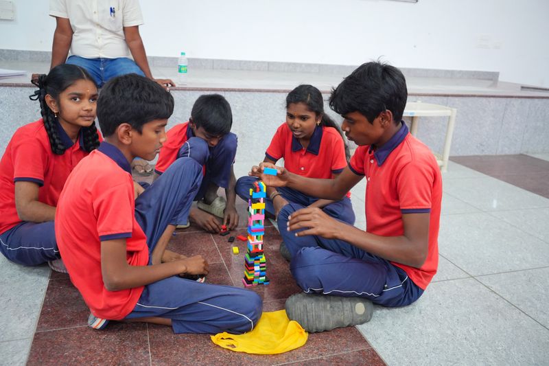 Students sit in a circle building a block tower together during a Kaushalya team-building exercise.