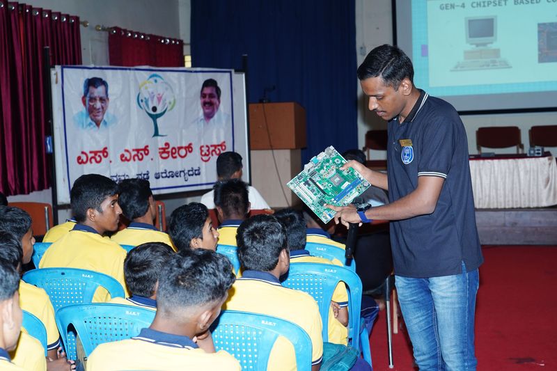 A facilitator shows students a computer circuit board while explaining hardware basics during a Kaushalya computer-skills session.