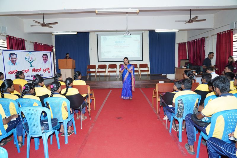 A facilitator speaks into a microphone in an auditorium aisle as students listen during a Kaushalya programme.