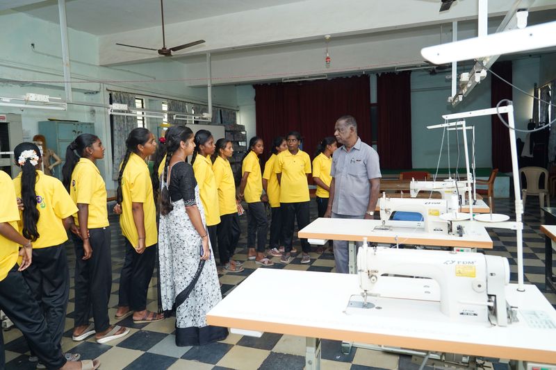 A facilitator talks with a line of students standing beside sewing machines during a Kaushalya skills visit.