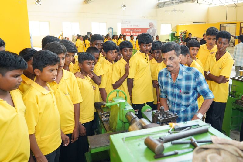 Students gather around an instructor demonstrating a workshop machine during a Kaushalya skills-training visit.