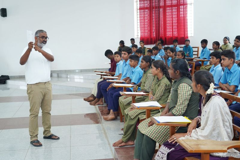A facilitator gestures while speaking to a group of seated students during a classroom awareness session.