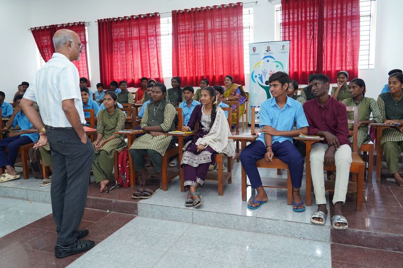 A speaker converses with a group of smiling students seated in rows during a legal-awareness session.