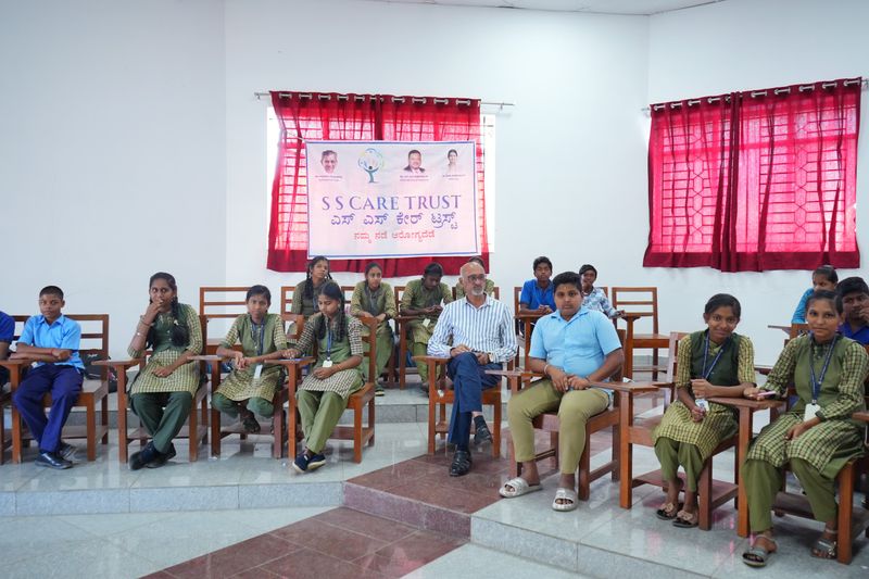 Students and a mentor seated in a semicircle beneath an S S Care Trust banner during a program session.