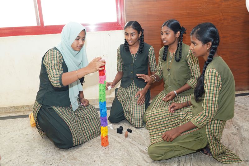 Four girls kneel together building a colorful block tower as part of a team-building activity.