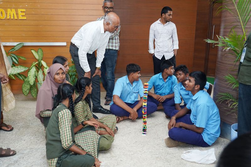 Mentors observe as students build a block tower together during a team activity near the entrance hall.
