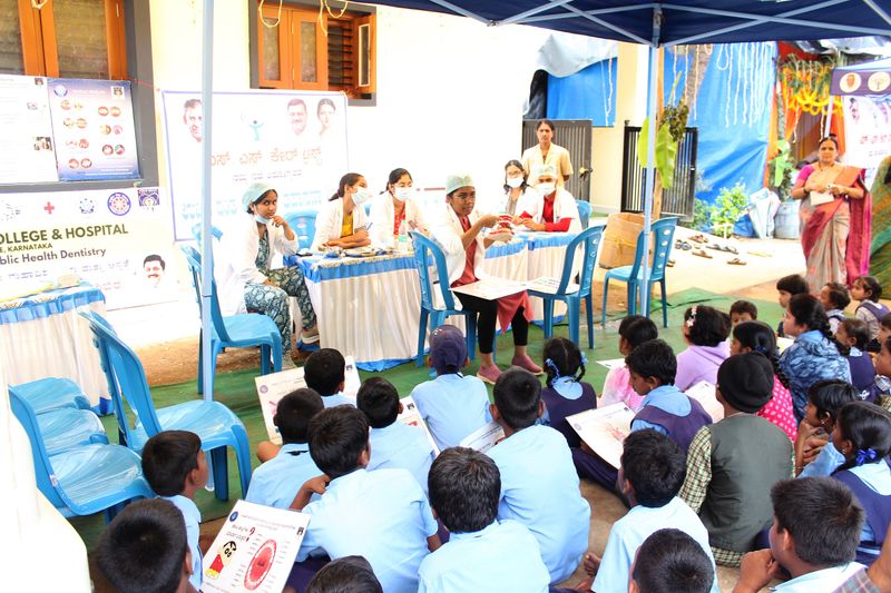 Students holding dental awareness charts listen as health workers from a dental college address them at a screening camp.