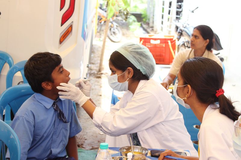 A health worker examines a schoolboy's mouth with a dental instrument during a free oral health screening camp.