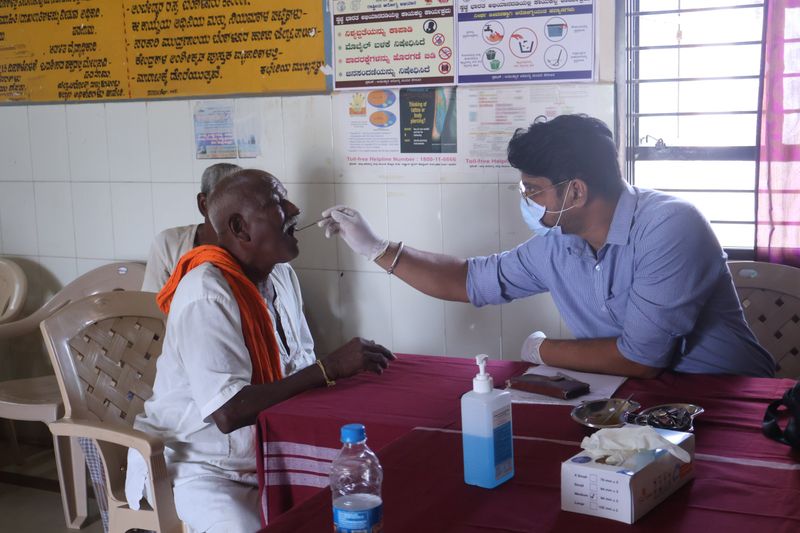 A health worker uses a tongue depressor to examine an elderly man's mouth during a dental screening camp.
