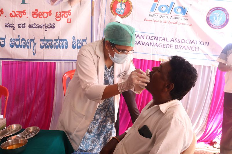 A masked dentist examines a seated man's mouth at a free dental camp held with the Indian Dental Association.