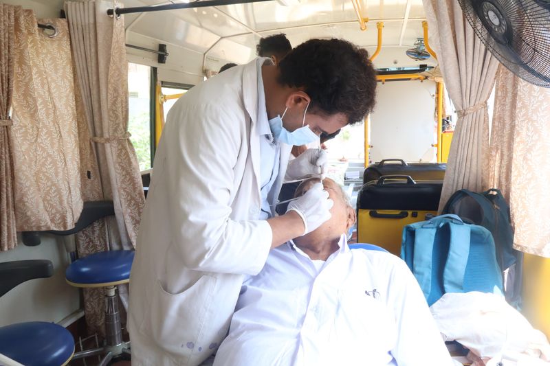 Inside a mobile dental van, a dentist examines an elderly man's mouth during a community screening.