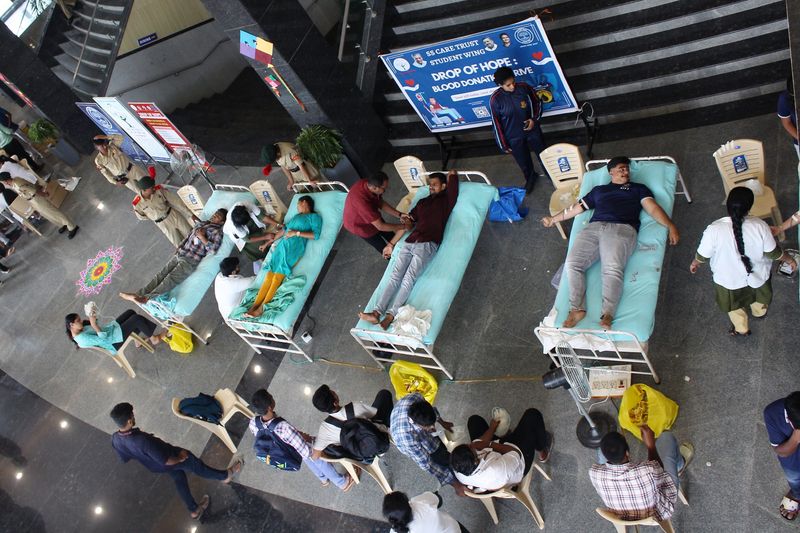 An overhead view of a blood donation drive with several donors resting on cots beside a Drop of Hope banner.