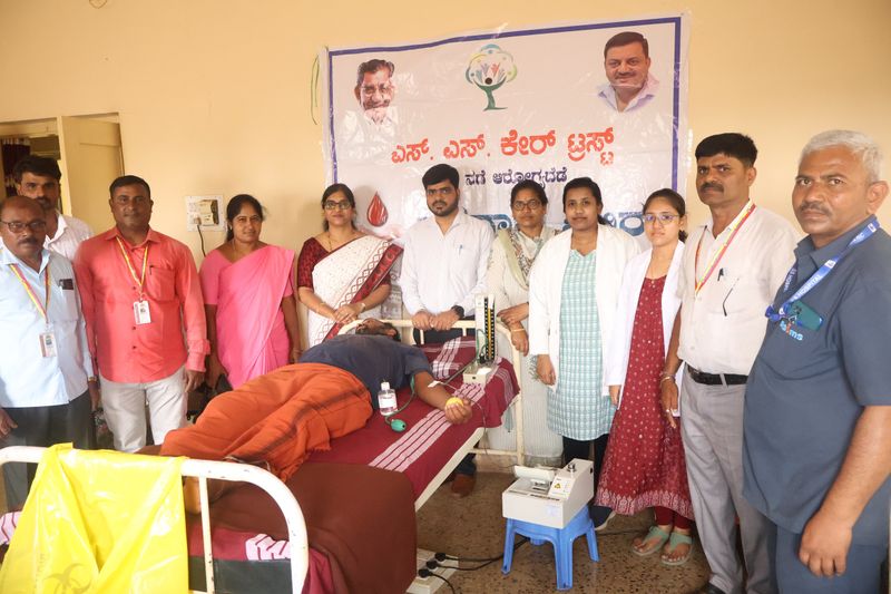 Staff, doctors and a blood donor pose together in front of the SS Care Trust banner during a blood donation camp.