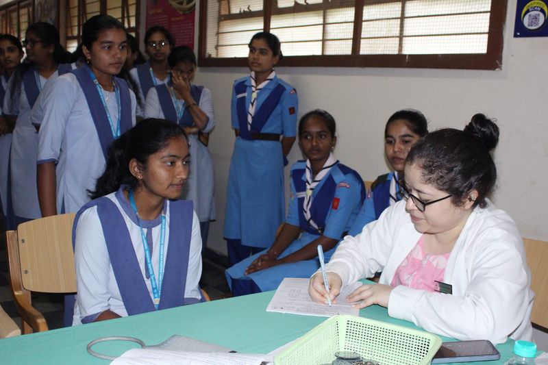 A staff member fills out a form at a registration table while college students in uniform look on during the campaign.
