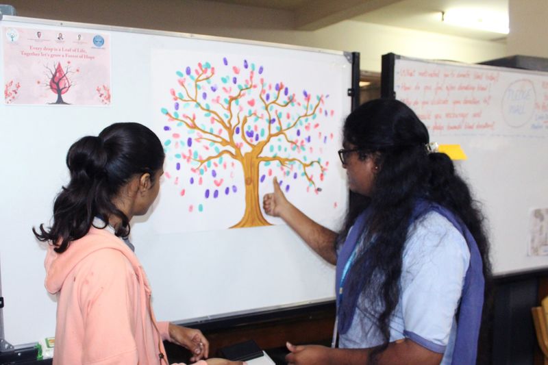 Two students look at a thumbprint tree poster reading 'Every drop is a Leaf of Life' during the pledge campaign.