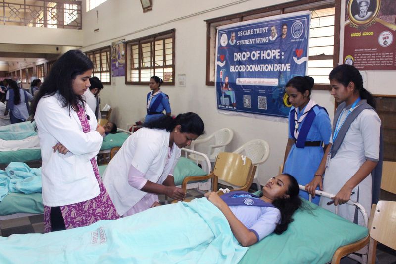 Doctors attend to a blood donor on a camp bed while students look on inside the Drop of Hope donation hall.