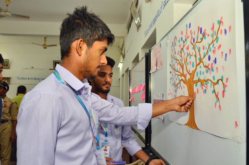 Two young men examine a thumbprint tree pledge poster for the blood donation awareness campaign.