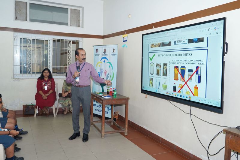 A speaker points to a screen titled "Let's choose healthy drinks", which crosses out sugary and energy drinks.