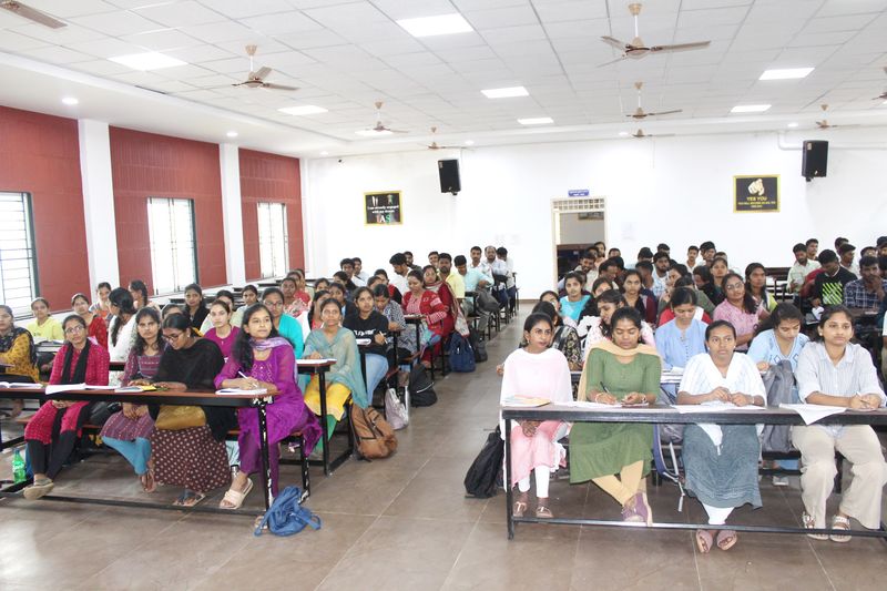 Young adult students take notes at long desks in a large classroom during a Sankalpa coaching session.