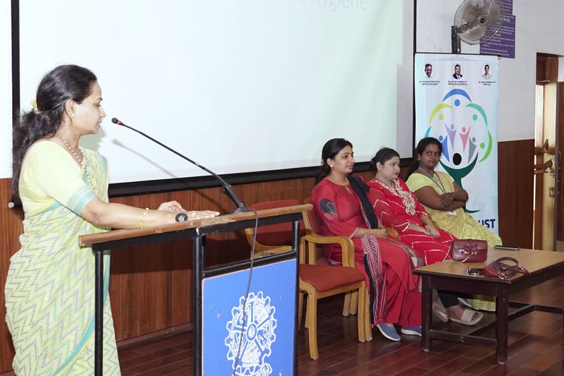 A speaker addresses an audience from a podium beside three seated women at a women's health seminar.