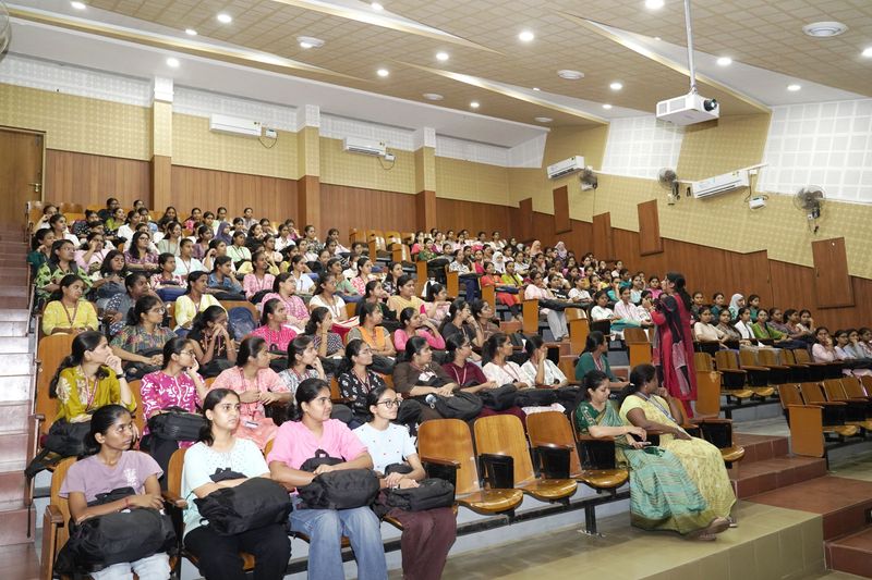 Rows of young women fill a large hall, attending a women's health awareness talk.